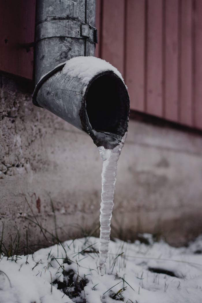 Watford Plumbing FAQs: Solving Dripping Taps, Burst Pipes & Toilet Overflows 1 Frozen drain spout with icicle against a snowy backdrop. Captured in Estonia.